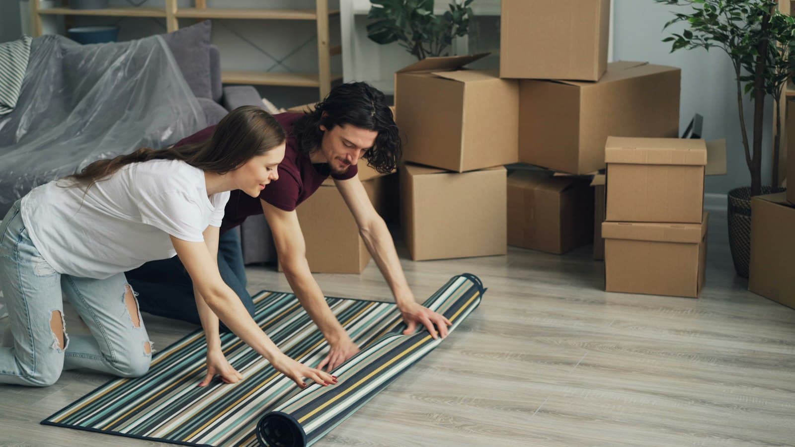 Couple unrolling a rug among moving boxes in a new home