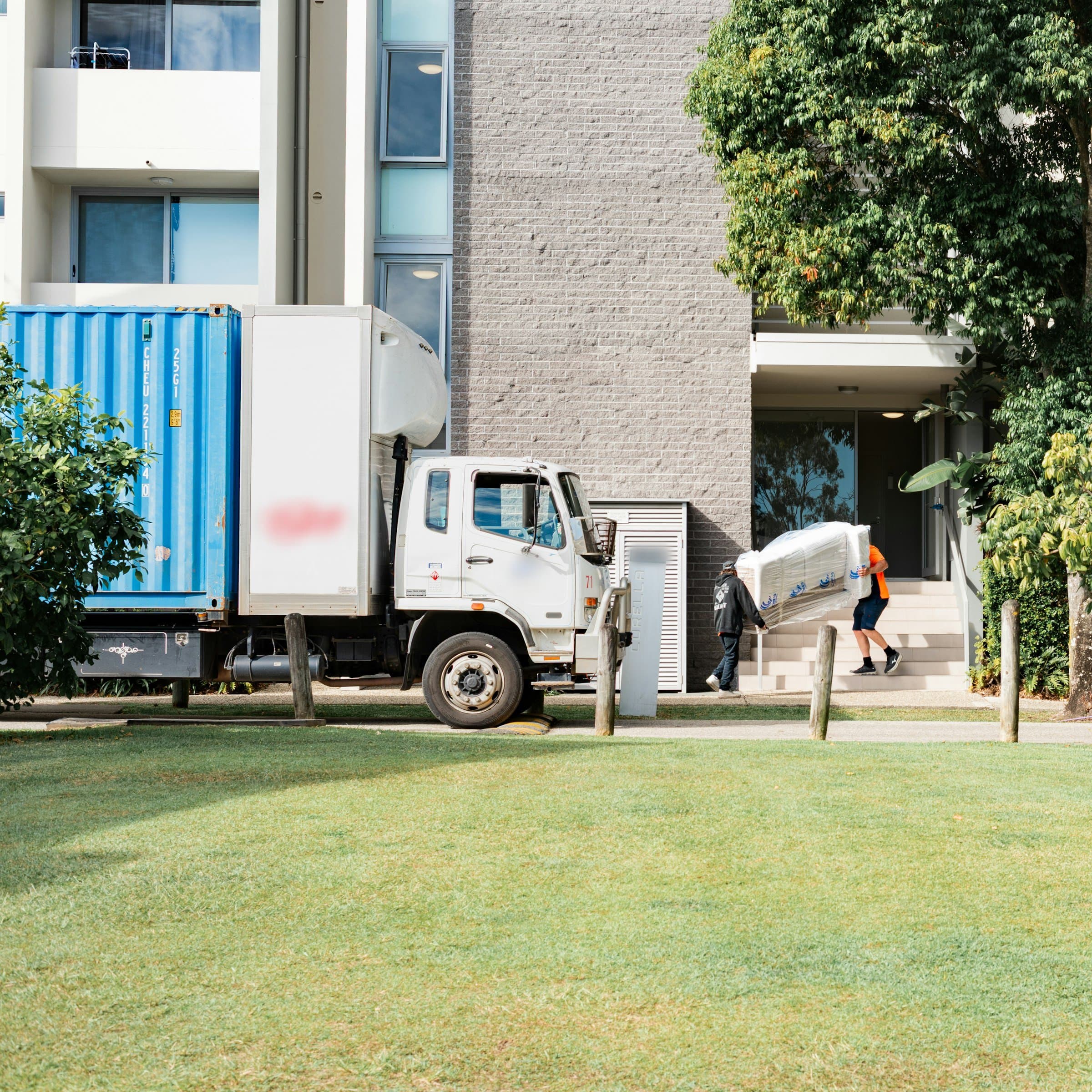 Movers carrying wrapped furniture from a moving truck into an apartment building